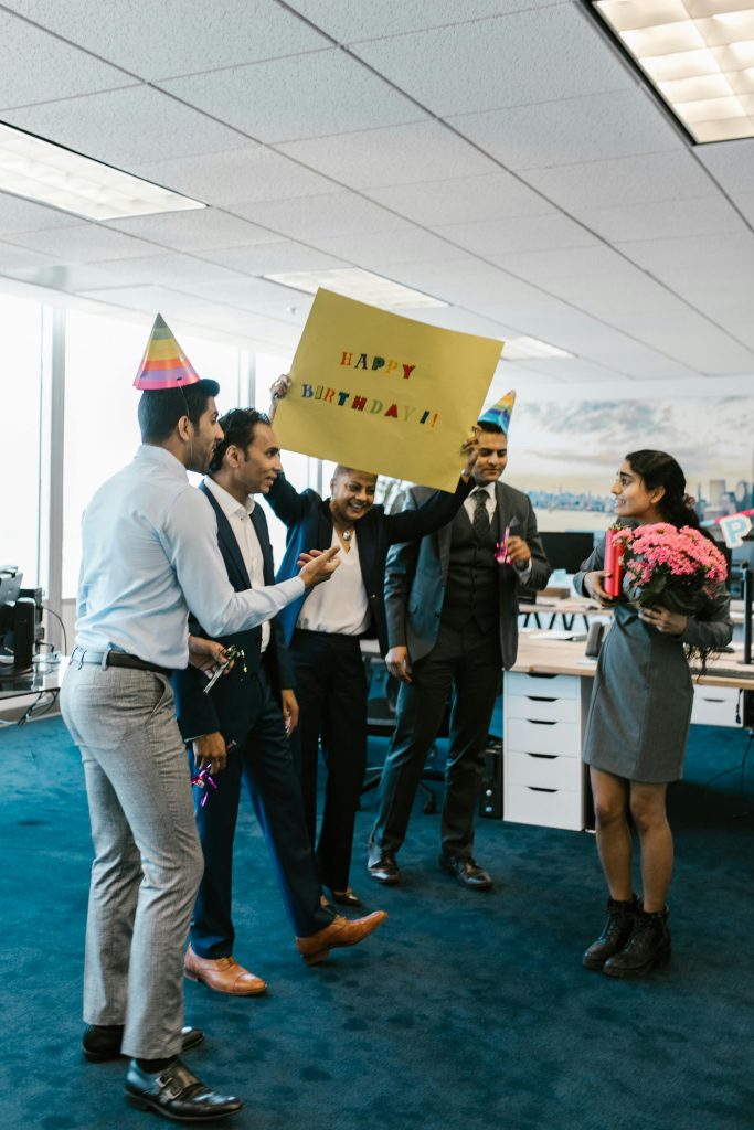 A joyous office birthday celebration with colleagues surprising a coworker with a sign and flowers.