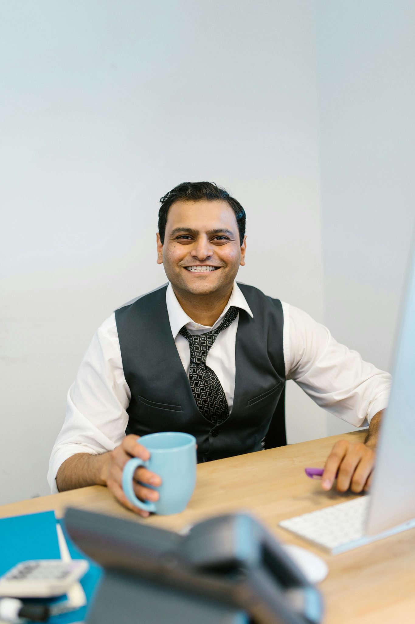 Cheerful businessman taking a coffee break at his office desk with a smile.