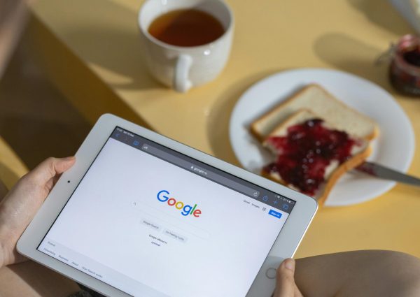 Person using a tablet with Google search open while having breakfast with toast and tea.
